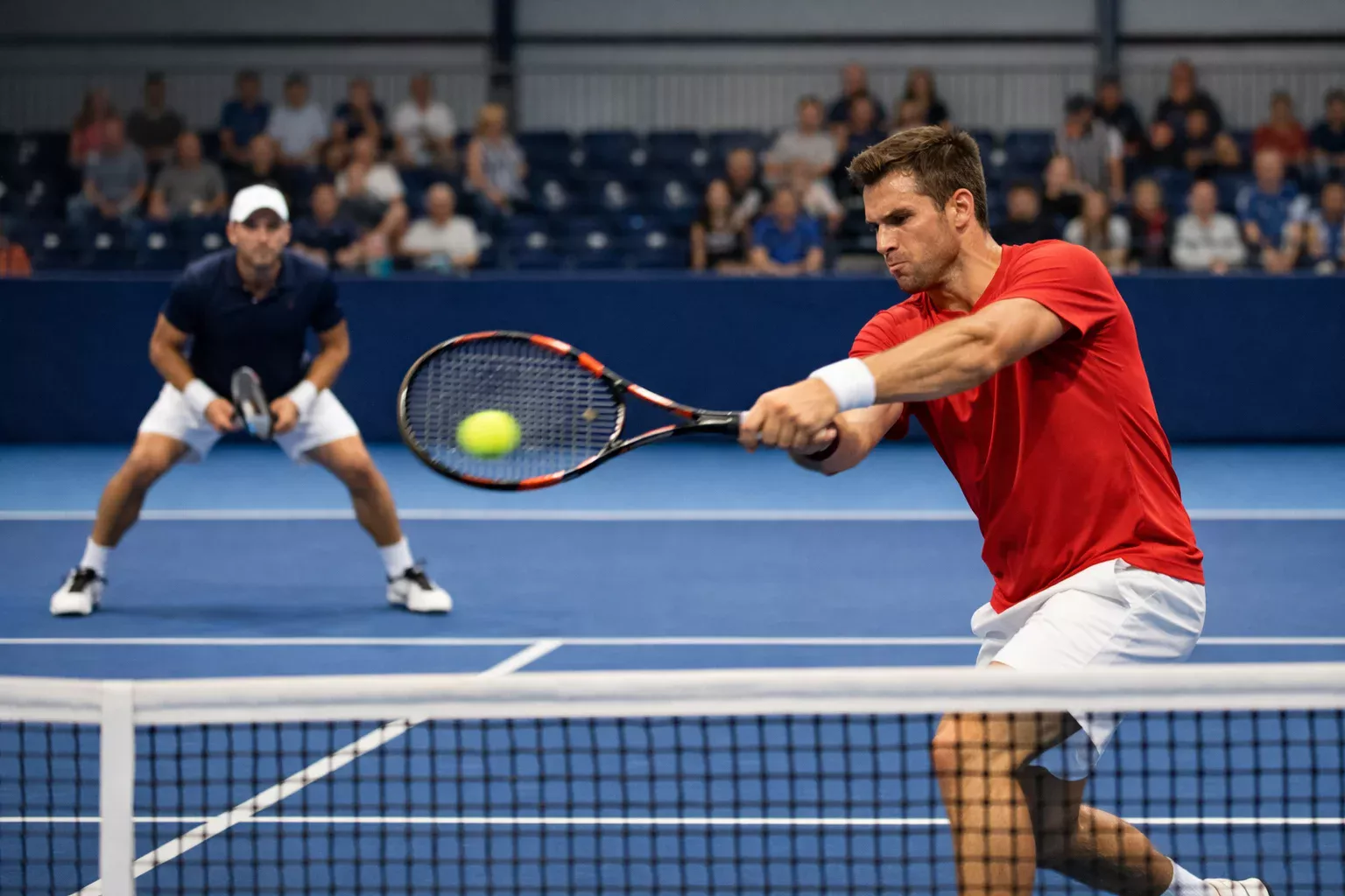 Match di tennis su cemento indoor con due giocatori in azione